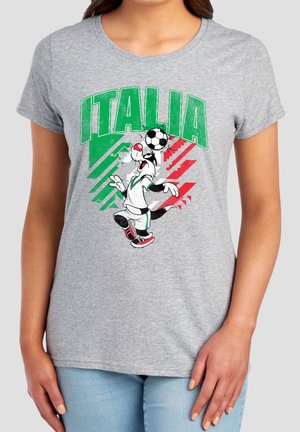 Frau trägt ein graues T-Shirt mit grünem und rotem Italien-Schriftzug und einer Comicfigur, die einen Fußball auf dem Kopf balanciert.