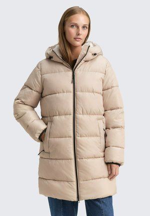 Veste rembourrée beige avec capuche, design matelassé, fermeture éclair et poches latérales. Présente un matériau texturé et des accents noirs au niveau des poignets.