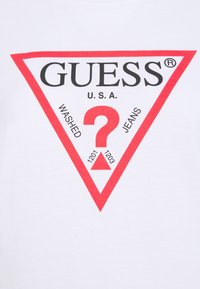 Hvid bomulds t-shirt med et stort rødt trekantlogo, der indeholder teksten "GUESS U.S.A." og "WASHED JEANS" samt et spørgsmålstegn i midten.