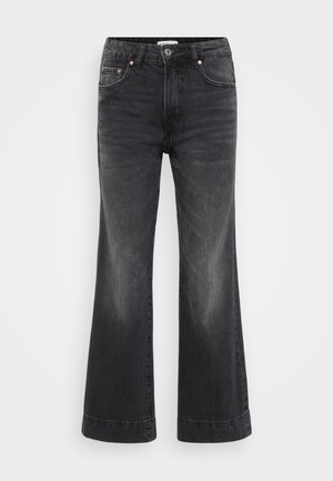 Pantalones vaqueros negros de pierna ancha con cintura alta, hechos de denim. Presentan bolsillos frontales, remaches de cobre y costuras visibles a lo largo de los dobladillos.