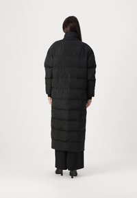 Sort puffy jakke med et langt, lige design. Har vandret quiltede sektioner, høj krave og minimalistisk stil.
