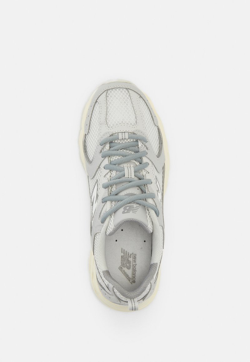 Chaussure de sport grise avec une tige en maille, fermeture à lacets, languette rembourrée et semelle texturée. Présente un logo sur le côté et sur la languette.