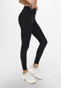Leggings neri a vita alta con pannelli cuciti e tasche laterali, realizzati in tessuto elasticizzato. Abbinati a sneakers bianche chunky.
