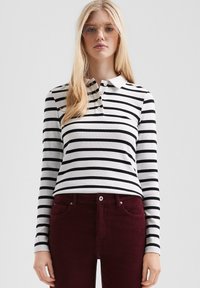 Zwart-wit gestreepte lange mouwen polo met een kraag en een drieknoopsluiting, gecombineerd met bordeauxrode corduroy broek.