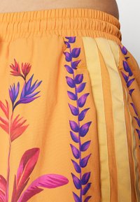 Oransje stoffshorts med livlige lilla og rosa blomstertrykk. Inkluderer gule sidestriper og elastisk midjebånd for komfort.
