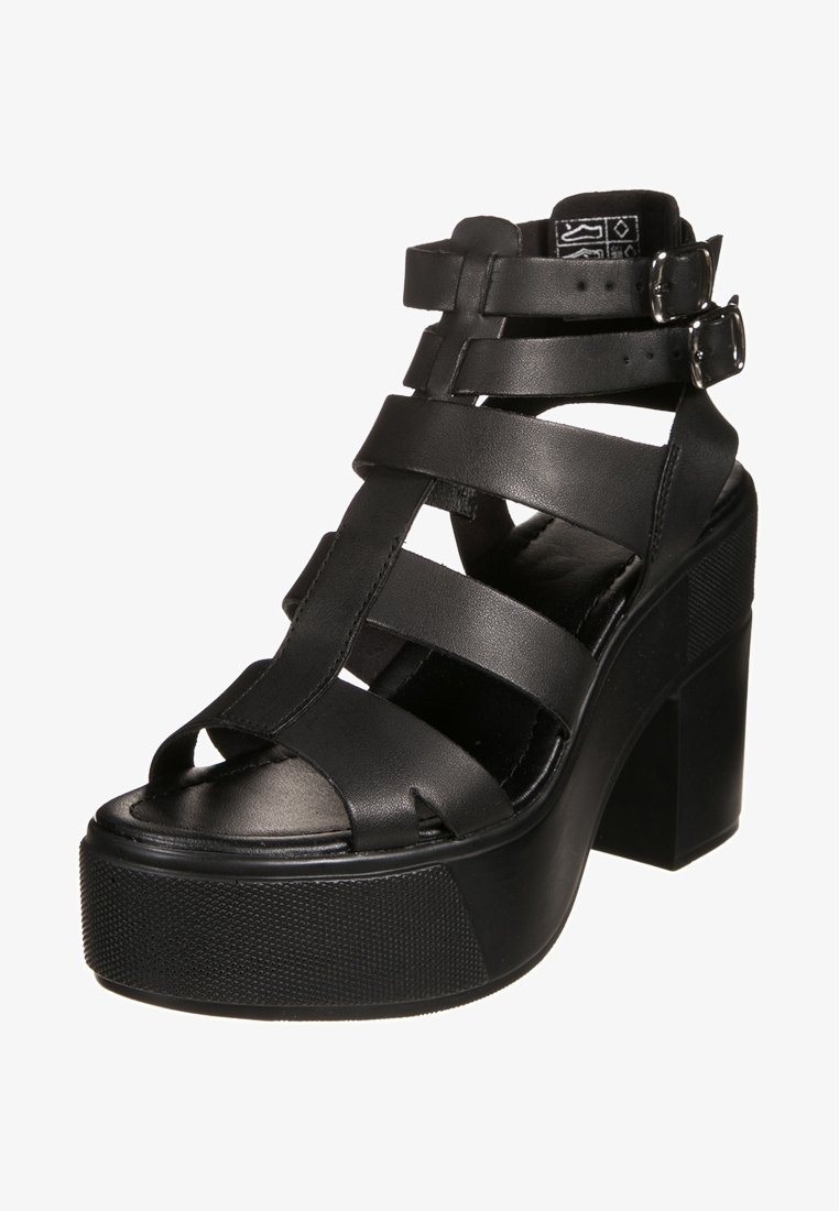 Sandale noire à plateforme haute avec talon épais, plusieurs brides sur le pied et fermeture à double boucle à la cheville.