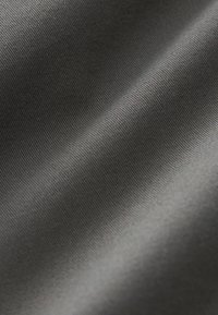 Gros plan sur un tissu lisse gris foncé avec une texture côtelée diagonale subtile et une lumière douce créant de délicates ombres à la surface.
