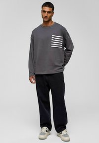 Grijze langemouwen sweatshirt met een gestreepte patch pocket, gecombineerd met zwarte losse broek en witte sneakers. Eenvoudig ontwerp en comfortabele pasvorm.