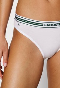 Fehér pamut alsónadrág zöld és fehér csíkos elasztikus derékpánttal, az oldalon egy kis Lacoste logó címkével.