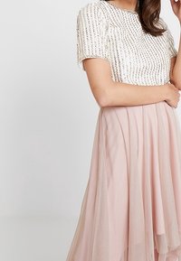 Rosa tyllkjol med en åtsittande vit topp som har vertikala pärlbroderier. Toppen har korta ärmar och rund halsringning.