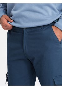 Granatowe spodnie cargo wykonane z mieszanki bawełny, z zamkiem błyskawicznym, przednimi kieszeniami oraz kieszenią boczną z zamkowym detalem.