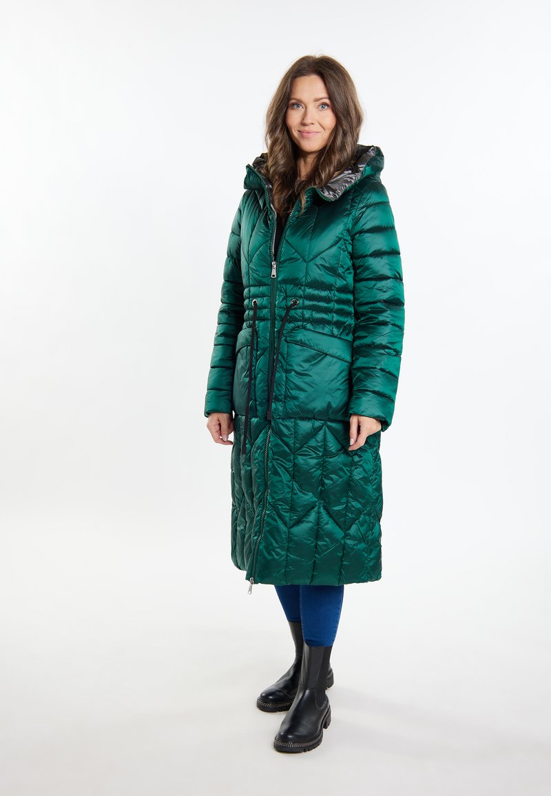 Cappotto imbottito verde con cuciture a rombi, dotato di cerniera frontale, vita regolabile con cordino e cappuccio. Presenta una finitura lucida e un motivo a diamante. Indossati stivali neri.