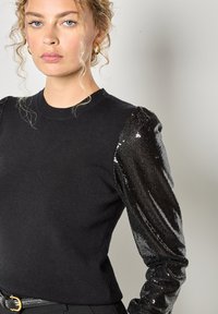 Czarny dzianinowy top z teksturowanymi długimi rękawami pokrytymi czarnymi cekinami, z klasycznym okrągłym dekoltem i dopasowanym krojem.