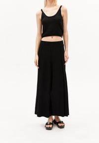 Débardeur noir court et pantalon noir large. Texture tricot lisse, taille élastique, sandales compensées noires à enfiler.