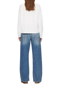 Top blanco de manga larga con un corte relajado, combinado con jeans azul de tiro alto y pierna ancha que presentan desvanecidos y bolsillos traseros.