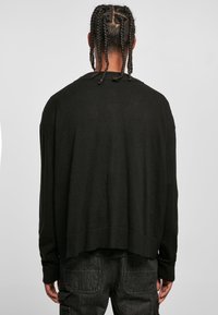 Czarny, oversize sweter o miękkiej fakturze, z szerokim dekoltem i obniżonymi ramionami, zestawiony z ciemnymi spodniami cargo.