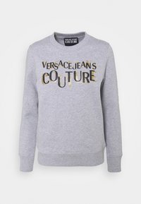 Light grey long-sleeve sweatshirt with ribbed cuffs and hem, featuring "Versace Jeans Couture" text in mixed black and gold glitter font on front.