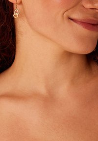 Boucles d'oreilles dorées en forme de deux cœurs entrelacés ; l'un est orné de petits strass clairs. Design léger et délicat.