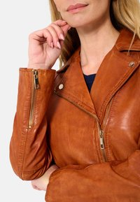 Braune Leder-Motorradjacke mit Reißverschluss und Druckknopfverschluss. Bemerkenswerte Textur mit einem leicht abgetragenen Finish, figurbetontes Design.