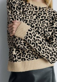 Beige svetr s černým leopardím vzorem, žebrovanými manžetami a lemem. Měkká pletenina, uvolněný střih a dlouhé rukávy.