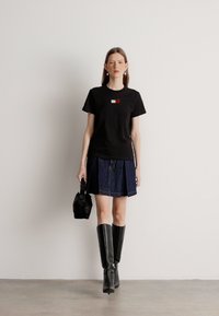 Czarny t-shirt z kolorową grafiką, dżinsowa spódnica, czarne kozakie do kolan oraz mała czarna torebka. Prosty, nowoczesny design z kontrastującymi teksturami.