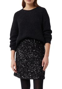 Schwarzer Strickpullover mit Rippenstruktur, kombiniert mit einem schwarzen Pailletten-Minirock mit glänzender, reflektierender Oberfläche.