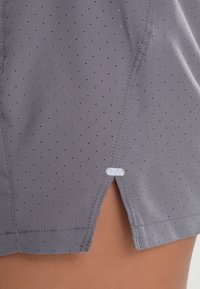 Pantalones cortos deportivos grises hechos de tela transpirable, con pequeñas perforaciones, un corte recto y una abertura lateral con un acento blanco.