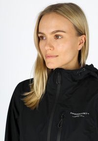Black waterproof jacket with a high collar, adjustable hood, and zippers. Features a logo on the chest and a smooth fabric texture.