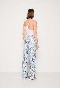 Lichtpaarse mouwloze top met een open rug, gecombineerd met losse bloemenprint broeken in pasteltinten met groene, roze en paarse accenten.