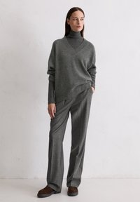 Oversized sweter w kolorze ciemnoszarym z dekoltem w serek, w zestawie ze dopasowanymi szarymi spodniami w kraty i brązowymi zamszowymi butami. Miękka tekstura i luźny krój.