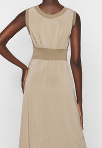 Robe sans manches beige avec un col et une taille côtelés. Texture lisse avec un corsage ajusté et une jupe fluide. Aucun motif visible.