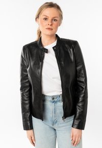 Zwarte leren jas met een ronde hals, ritssluiting aan de voorkant en lange mouwen. Draagt over een wit shirt en gecombineerd met hoge taille blauwe spijkerbroek.