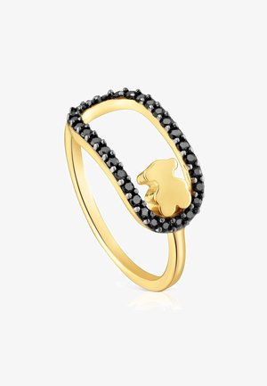 Anneau en or avec un sommet ovale ouvert bordé de petites pierres noires et une petite forme d'ours en or à l'intérieur de l'ovale.