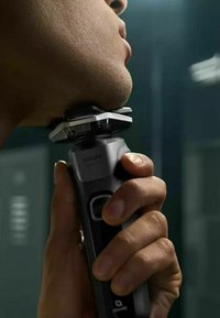 Rasoi elettrico Philips con un elegante corpo nero, rifiniture argentate e una testa a più lame, tenuto contro una mascella in un ambiente poco illuminato.