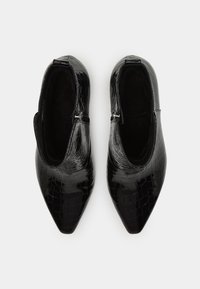 Paire de bottines noires à bout pointu avec texture croco et fermetures éclair latérales, vues de dessus sur un fond blanc.