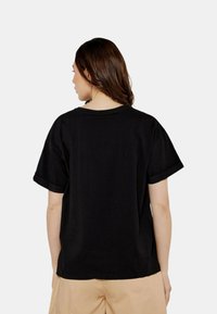 T-shirt in cotone nero con maniche corte e collo rotondo. La vista posteriore mostra una vestibilità rilassata e risvolti sulle maniche.