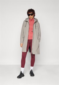 Lys grå vanntett jakke med hette, glidelås foran og snorjusteringer, over en rosa topp og bordeaux tights. Svarte sko og hvite sokker.