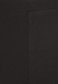 Schwarze Leggings aus einem glatten, dehnbaren Stoff mit einer körpernahen Passform. Die Textur wirkt weich mit minimal sichtbaren Nähten.