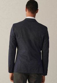 Tumesinine bleiser, mis on valmistatud tekstuurilisest kangast, slim-fit lõikega, klassikaliste kraedega ja pruuni nööpide aktsentidega, nähtaval tagant.