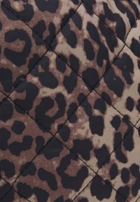 Tejido acolchado que presenta un patrón de estampado de leopardo en tonos marrón y beige con acentos negros sobre una textura suave. El diseño incluye un acolchado en forma de diamante.