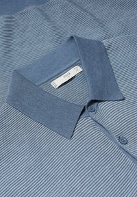 Polo shirt bleu clair avec une texture côtelée, patte de boutonnage et col contrastant. Il présente de fines rayures horizontales et une étiquette de marque.