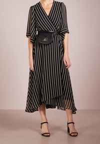 Musta-valkoinen raidoitettu kietaisumekko, jossa on leikatut hihat ja epäsymmetrinen helma, yhdistettynä pieneen mustaan vyökoteloon ja remmisiin korkokenkiin.