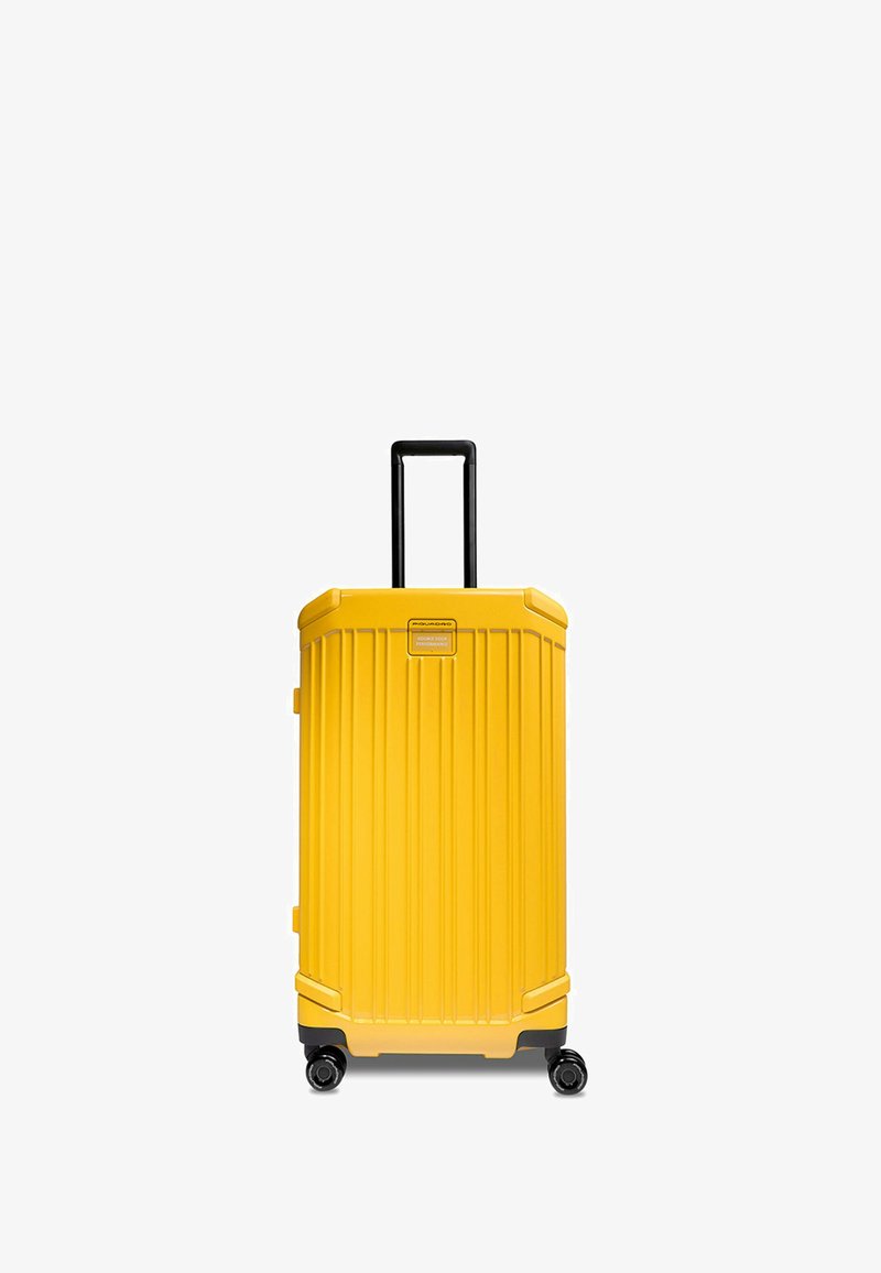 Valise rigide jaune avec des rainures verticales, poignée noire et quatre roues pivotantes pour une mobilité facile. Caractérisée par un design robuste et durable.
