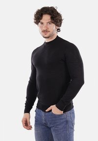 Maglietta nera a maniche lunghe, aderente, con una texture a coste, colletto alto e design senza cuciture sulle spalle, abbinata a jeans azzurri chiari.
