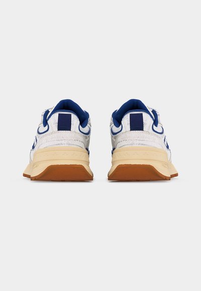 Baskets blanches avec des accents bleus, semelles intermédiaires beiges et semelles extérieures marron, vues de dos sur un fond blanc uni.