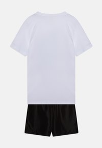 T-shirt en coton blanc à manches courtes et col rond, associé à un short noir en tissu lisse. Aucun motif ni détail visible.