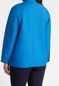 Niebieska kurtka o prostym kroju, z długimi rękawami i mankietami na guziki. Gładka faktura i jednolity wzór, bez ozdobnych motywów.