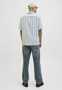 Chemise à rayures à manches courtes en blanc et bleu, associée à un jean en denim délavé à coupe loose. Inclut une casquette de couleur claire et des chaussures noires.