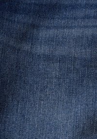 Tissu en denim bleu foncé avec une texture lisse et un motif en sergé diagonal, présentant des variations subtiles de teinte et d'intensité partout.