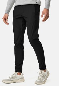 Svarta byxor i lätt material med slim fit och fyra fickor, kombinerade med krämfärgade sportskor.